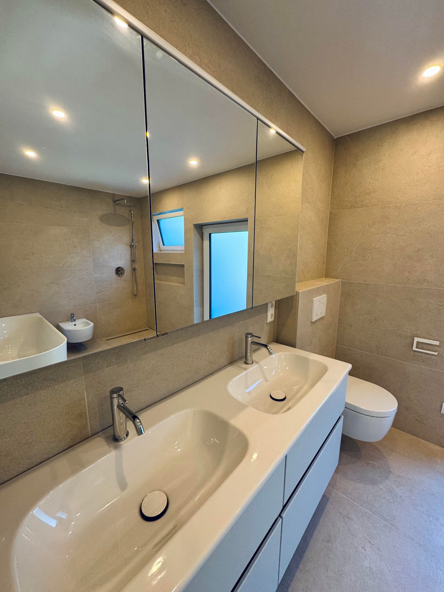 Badezimmer mit großformatigen Fliesen, Doppelwaschbecken und Spiegelschrank